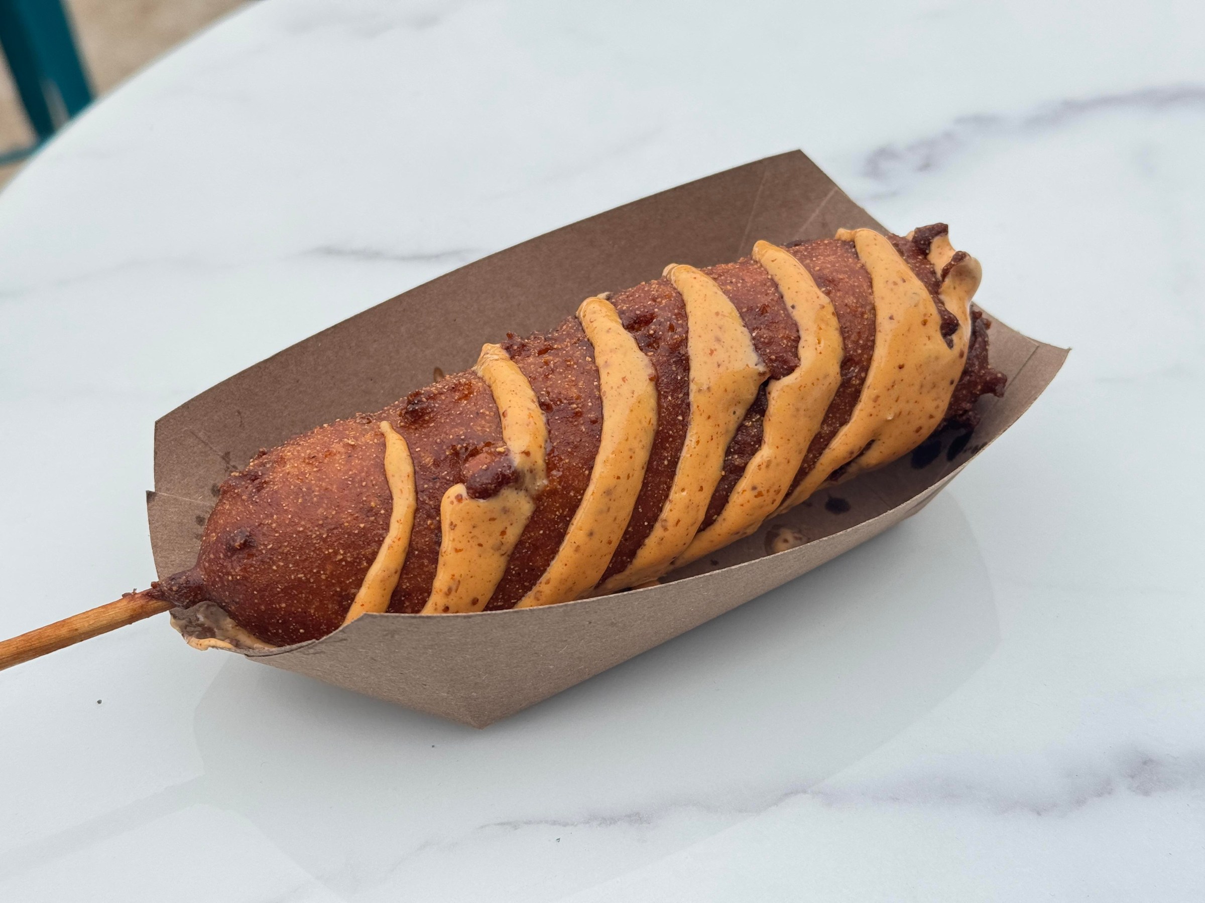 A corn dog with orange sauce in a paper tray from Sandy’s in San Francisco.