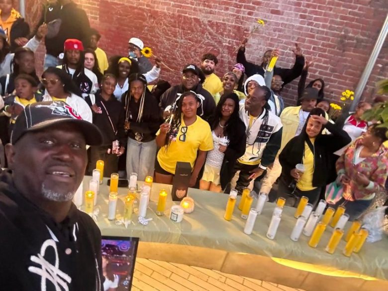 A group of people gathers around a table with lit candles and flowers, posing for a photo in front of a brick wall.