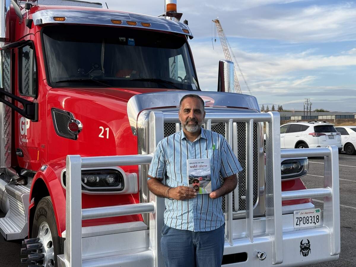 Gurinderjit Singh poses with his Peterbilt truck and a copy of his book in a yard in Fresno.