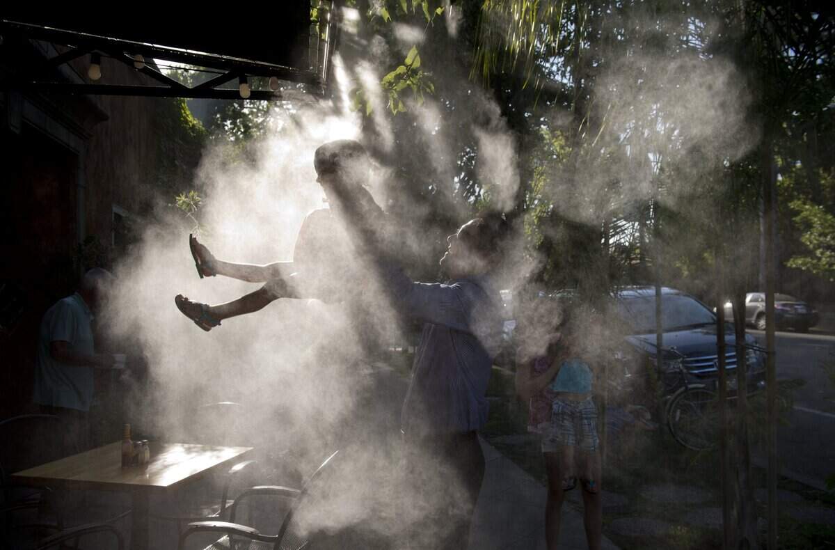Jesse Garcia lifts his daughter Presley Garcia, 4 into the water mist outside of Cafe Dantorels in Curtis Park