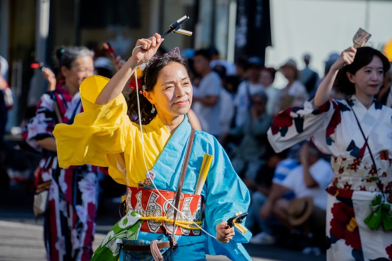 A parader holds a pair of wooden clappers, naruko, while dancing yosakoi in a vibrant yukata costume.