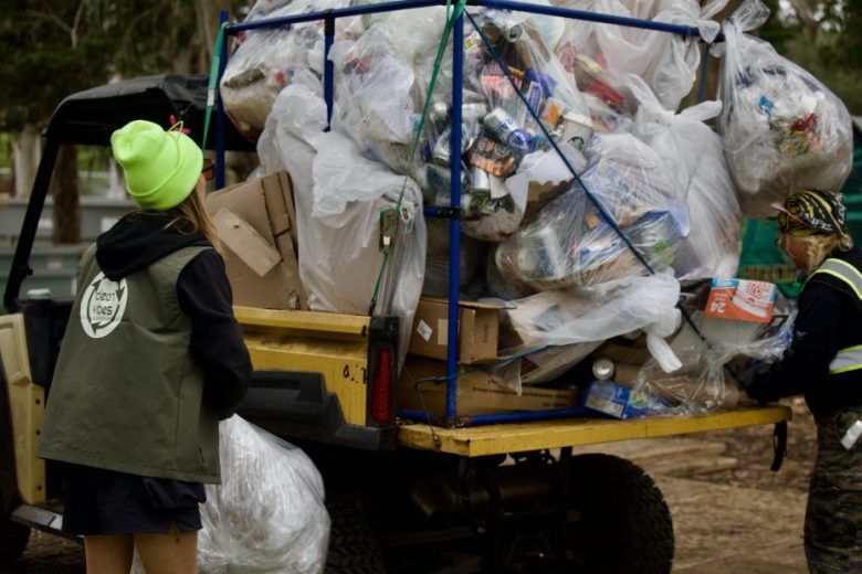 Two people load a vehicle with large bags of collected trash and recyclables during a cleanup effort in an outdoor area.