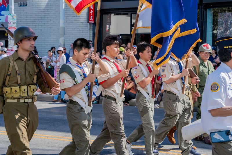 Youth scouts bear ceremonial flags alongside Nisei veterans in the parade lineup.