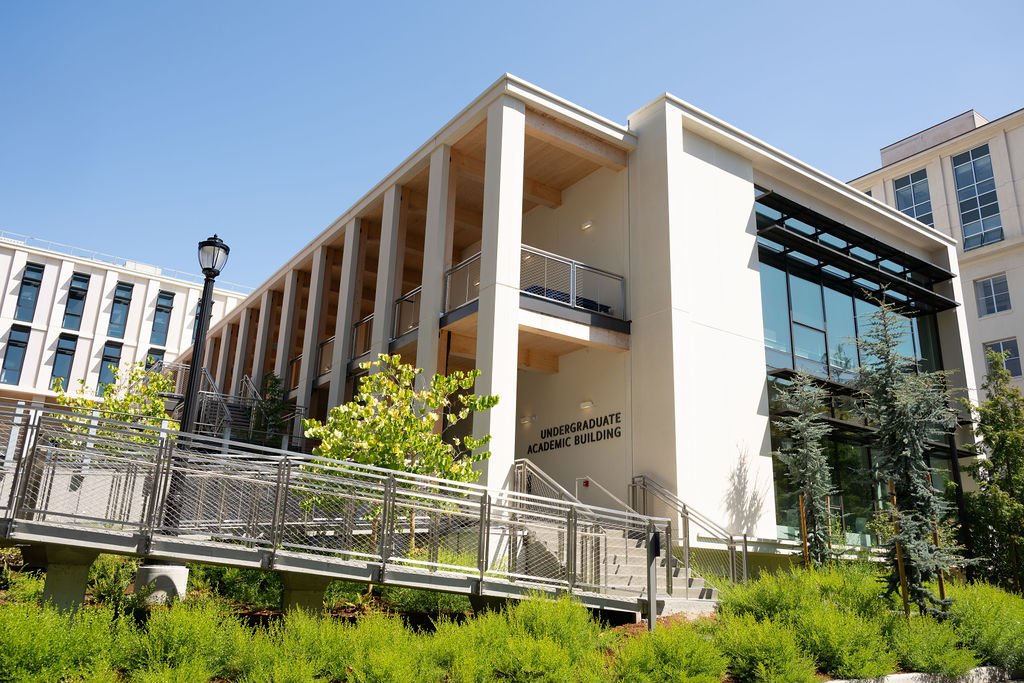 An exterior side view of the Undergraduate Academic building, showing a terrace with vibrant plants and an accessible entryway.