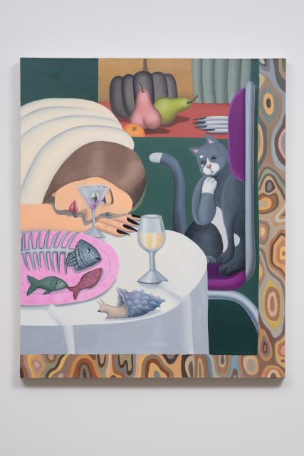A woman rests her head on a table beside a fish skeleton, wine glass, and martini, while a gray cat looks on; fruit and plates are in the background.