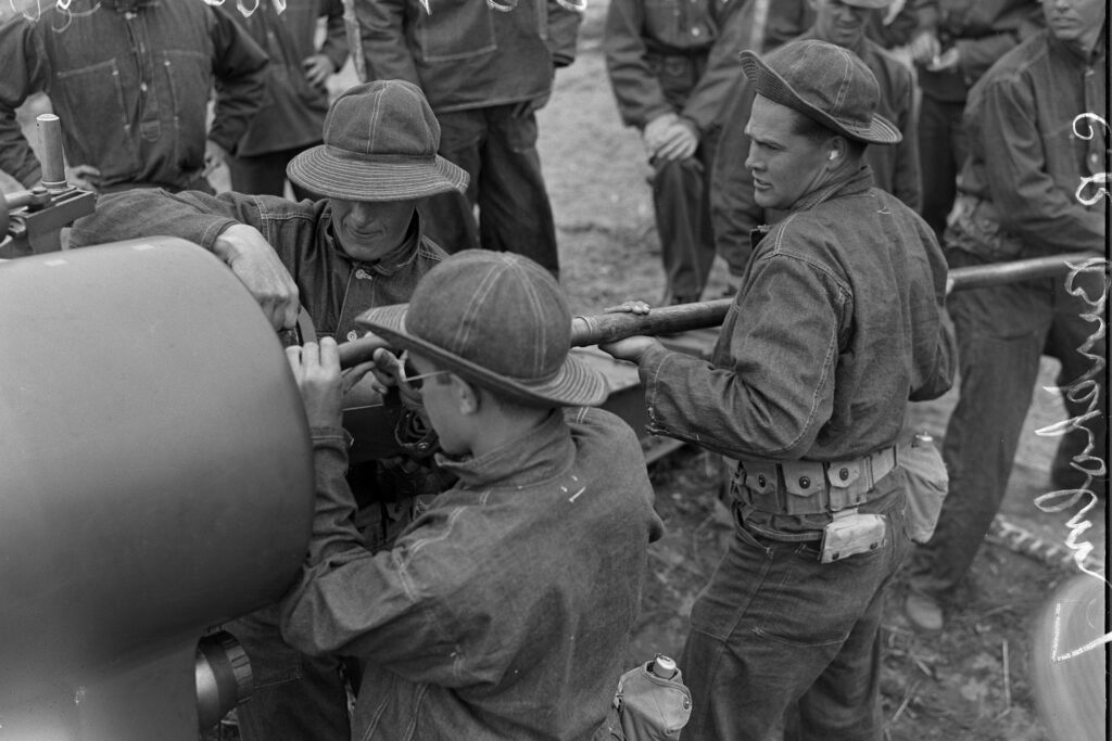 Three young men in military garb work at the base of a giant cannon in this black and white photo from 1938.