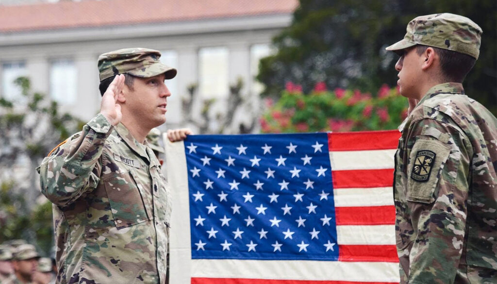 U.S. Army Lieutenant Colonel Aaron Elliott, at left, stands in front of a flag and salutes