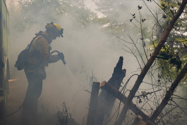 A firefighter sprays water on a hot spot from the Timber Fire above Deetjen's Inn in Big Sur, Calif., Tuesday, Aug. 11, 2026. (AP Photo/Nic Coury)