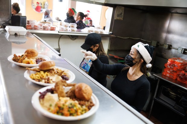 Volunteers including Gina Ferrer, right, prepare meals during Home of Chicken and Waffles' "Christmas Brunch" for local residents in need of hot meals near Jack London Square in Oakland on Dec. 25, 2023. The event was also sponsored by The City Eats and Black Owned Project 365. (Dai Sugano/Bay Area News Group)