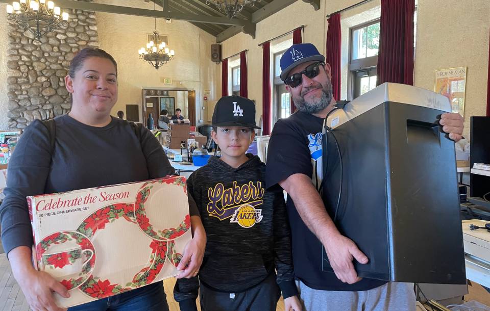 two adults and a teenage boy hold garage sale finds in a large hall