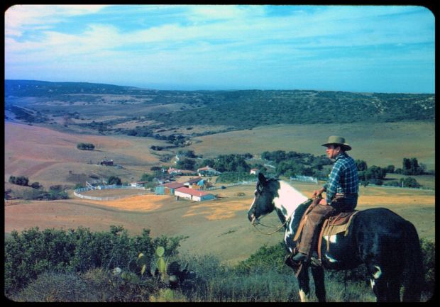 In a historic photo, Leo Carrillo surveys the property he bought in 1937 for a working ranch and private retreat. In the valley below, whitewashed adobe buildings stand out against the undeveloped Carlsbad hills. Set among wild chaparral and yucca, the ranch structures appear as a natural part of the rugged, open terrain. (Courtesy of city of Carlsbad, Carrillo Ranch Archive)