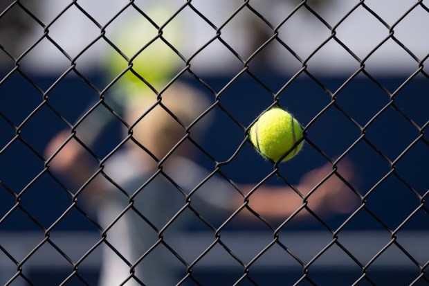 People practice on the court as a tennis ball sits stuck in the fence at the Barnes Tennis Center on Friday, Aug. 28, 2026, in San Diego. (Luke Johnson / The San Diego Union-Tribune)