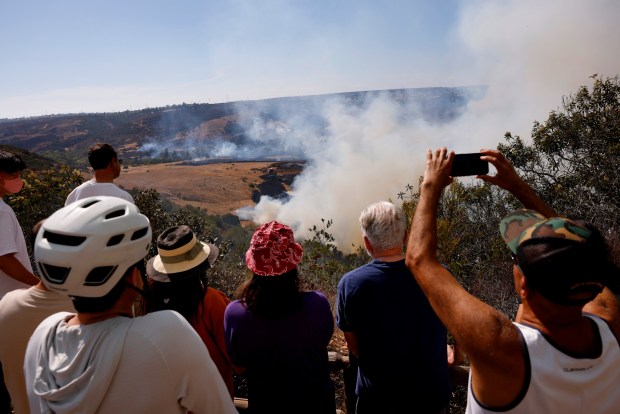 San Diego, CA - August 16: Local residents look on as firefighters battle a 130-acre brush fire in Los Peñasquitos Canyon Preserve on August 16, 2026 in San Diego, CA. (K.C. Alfred / The San Diego Union-Tribune)