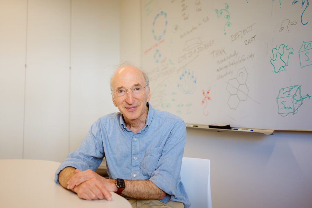 Saul Perlmutter seated in front of a white board with equations and drawings on it.