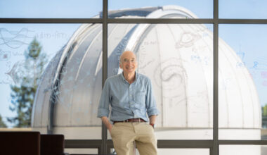Saul Perlmutter leans in front of a window with equations and drawings, with a telescope in the background.