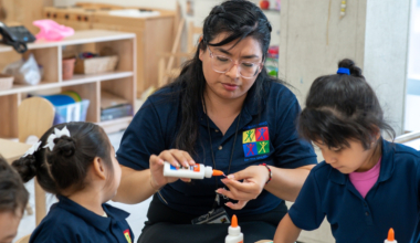 A Latina educator wearing clear-framed glasses and a navy polo shirt with a