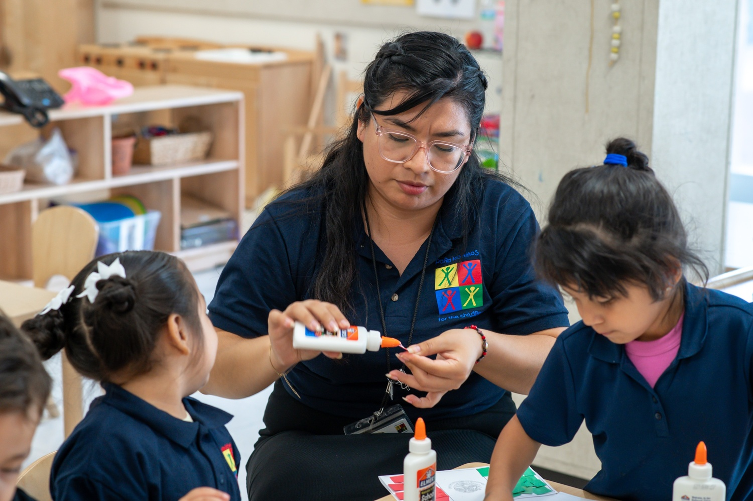 A Latina educator wearing clear-framed glasses and a navy polo shirt with a