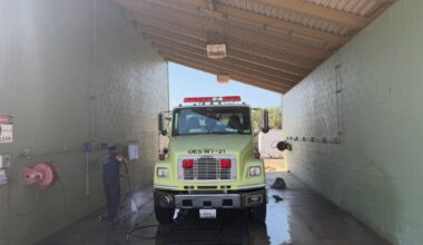 a firefighter washes a yellow fire truck in a bay.