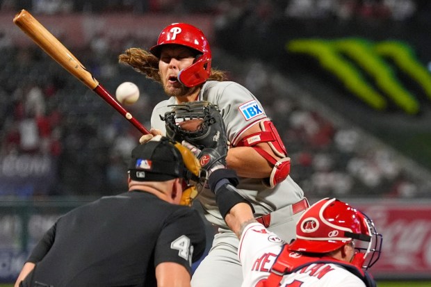 Philadelphia Phillies' Alec Bohm, center, is hit by a pitch as Los Angeles Angels catcher Tyler Heineman, right, and home plate umpire Shane Livensparger watch during the ninth inning of a baseball game Friday, Aug. 28, 2026, in Anaheim, Calif. (AP Photo/Mark J. Terrill)