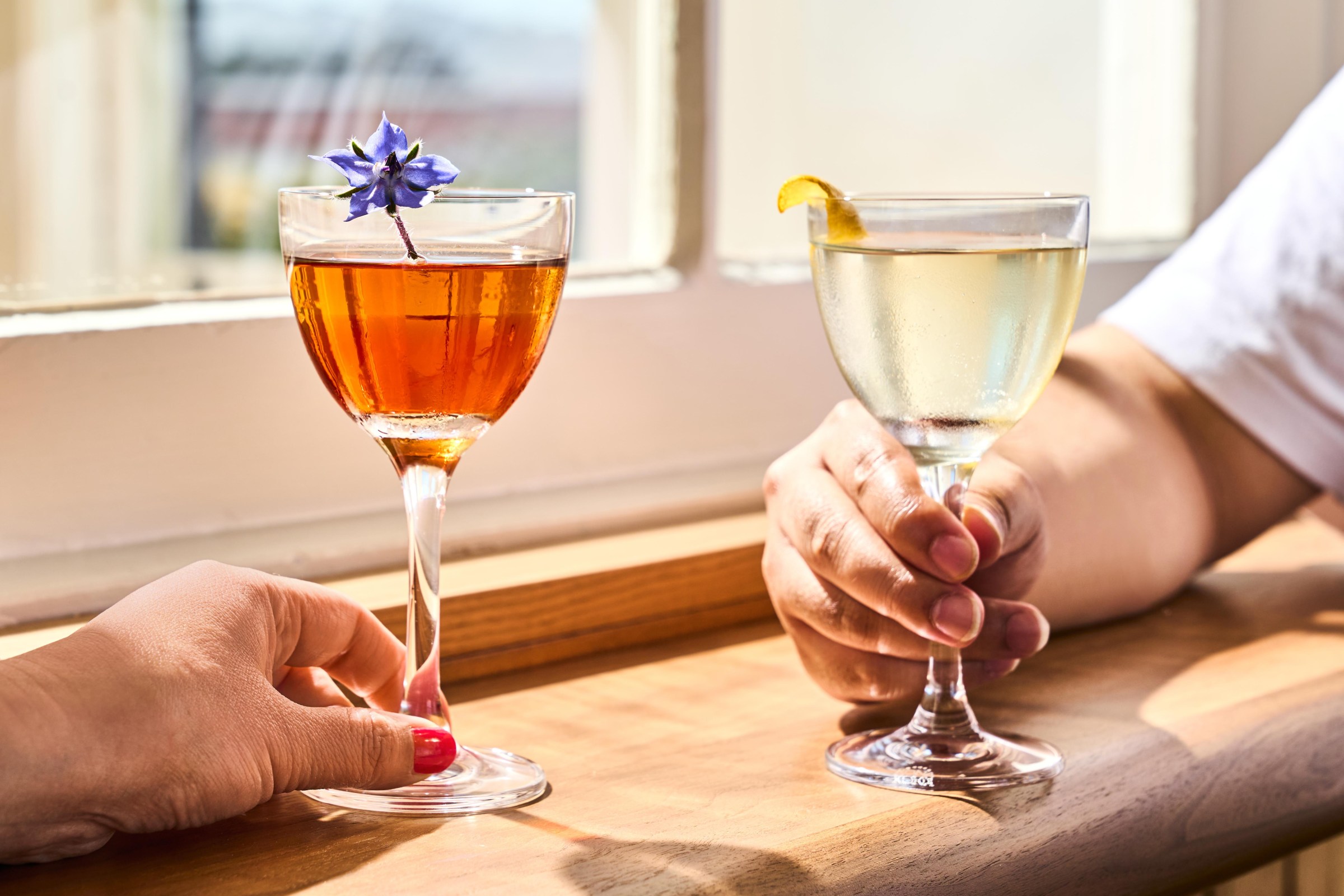 Two hands hold cocktails near a window at the Mess Hall in San Francisco.