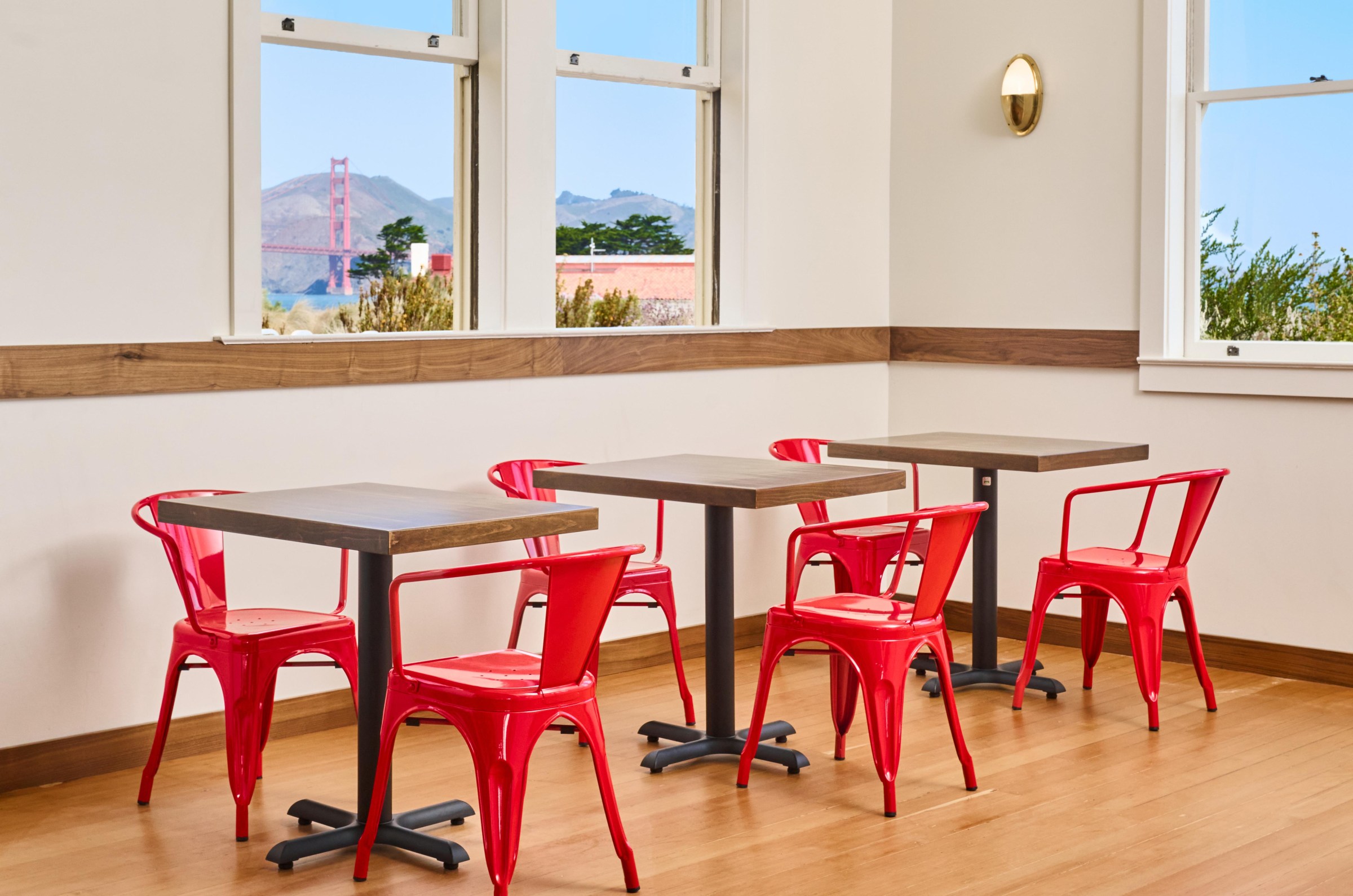 Three sets of tables and chairs at the Mess Hall in San Francisco, with a view of the Golden Gate Bridge seen out of the window.