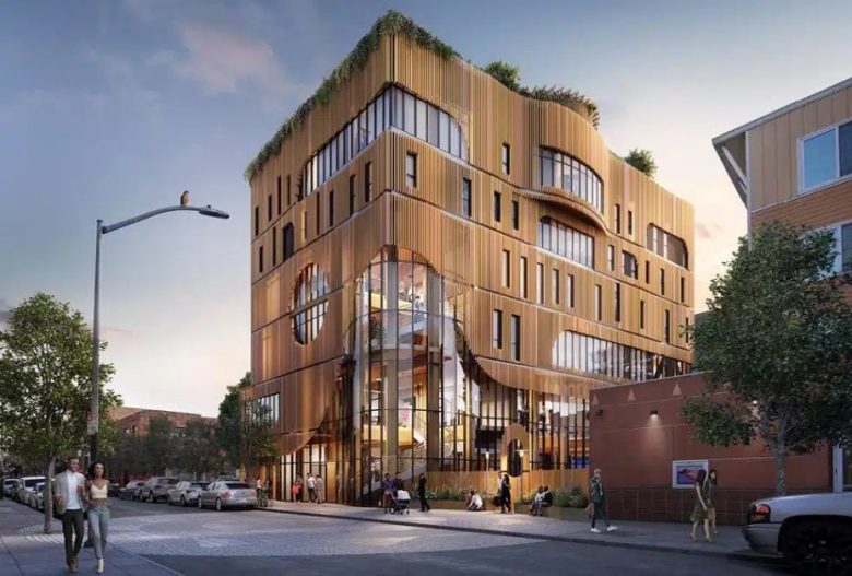 A modern multi-story building with curved golden exterior panels, large windows, rooftop greenery, and people walking nearby on a city street at dusk.