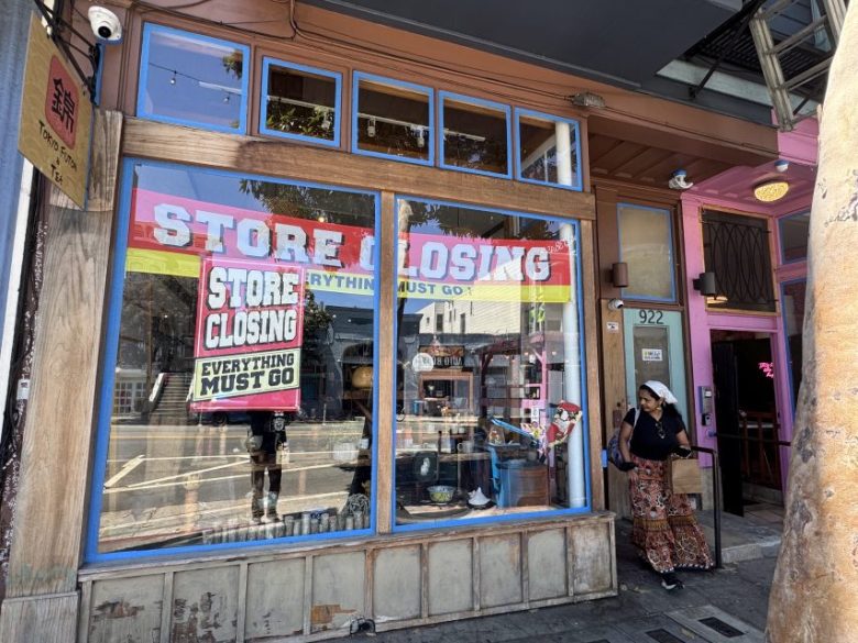 Storefront with large “Store Closing” and “Everything Must Go” signs in the window; shelves and items visible inside; a person exits the doorway onto the sidewalk.