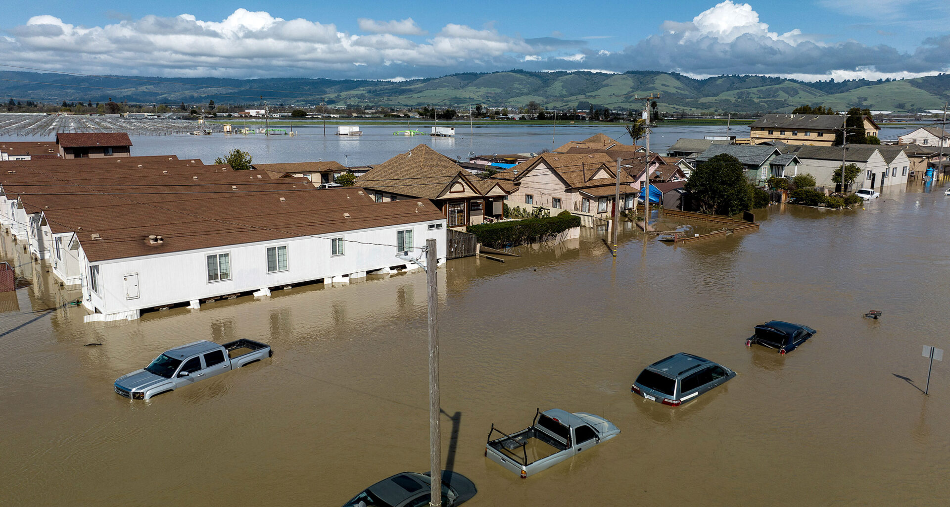 An aerial shot of houses, streets and cars completely submerged in brown flood water.