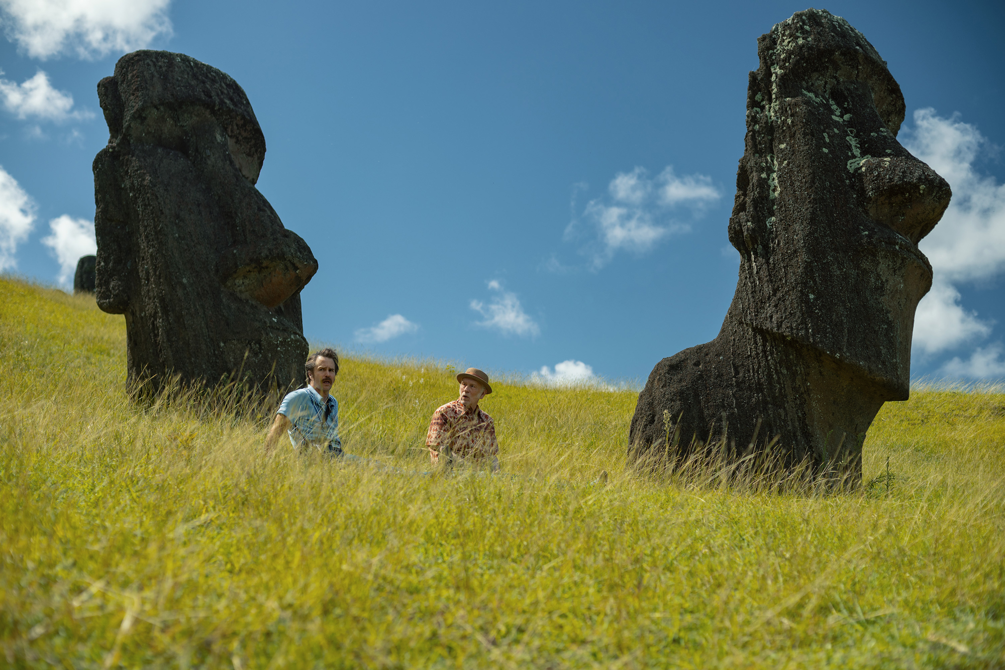 two men sit in grasses at foot of Easter Island head sculptures