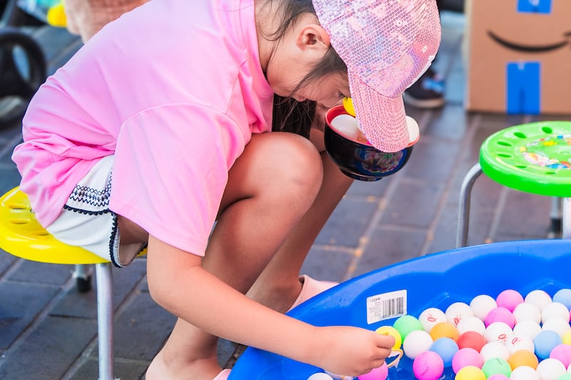 A young attendee tries to scoop table tennis balls to win redemption points at a game booth.