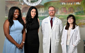 Onwodi Ifejeokwu, lead CAR T-cell study author Atena Zahedi, UC Irvine assistant professor of clinical pharmacy practice, Shawn Griffin and Dr. Erin Dean stand in front of a painting under a boom light