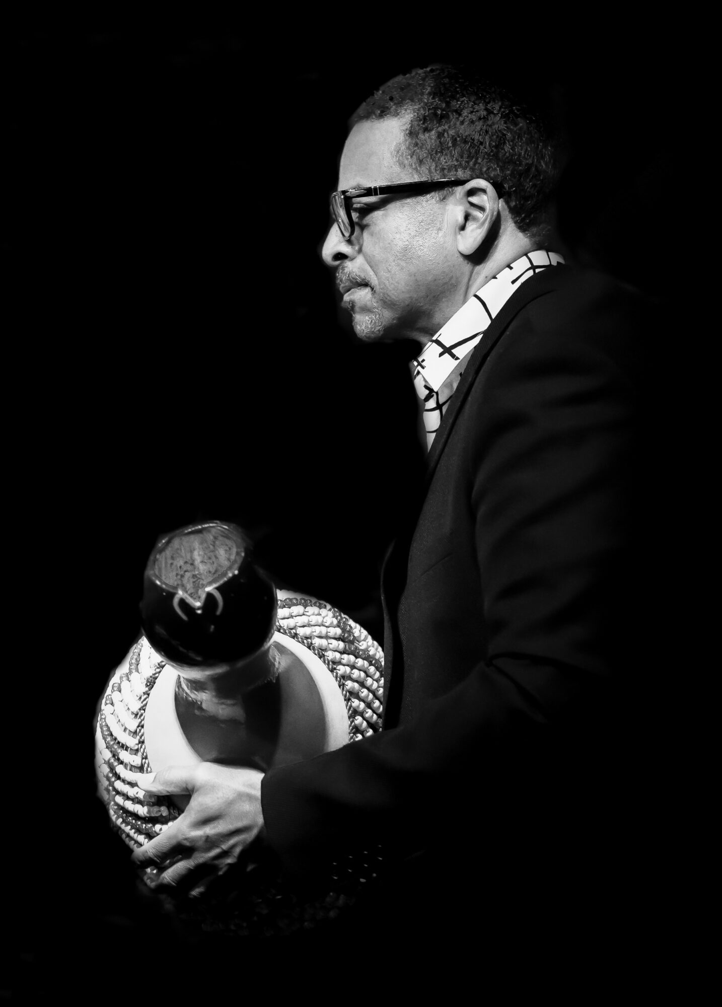 Man in glasses holding a ceramic vase, looking down, against a black background.