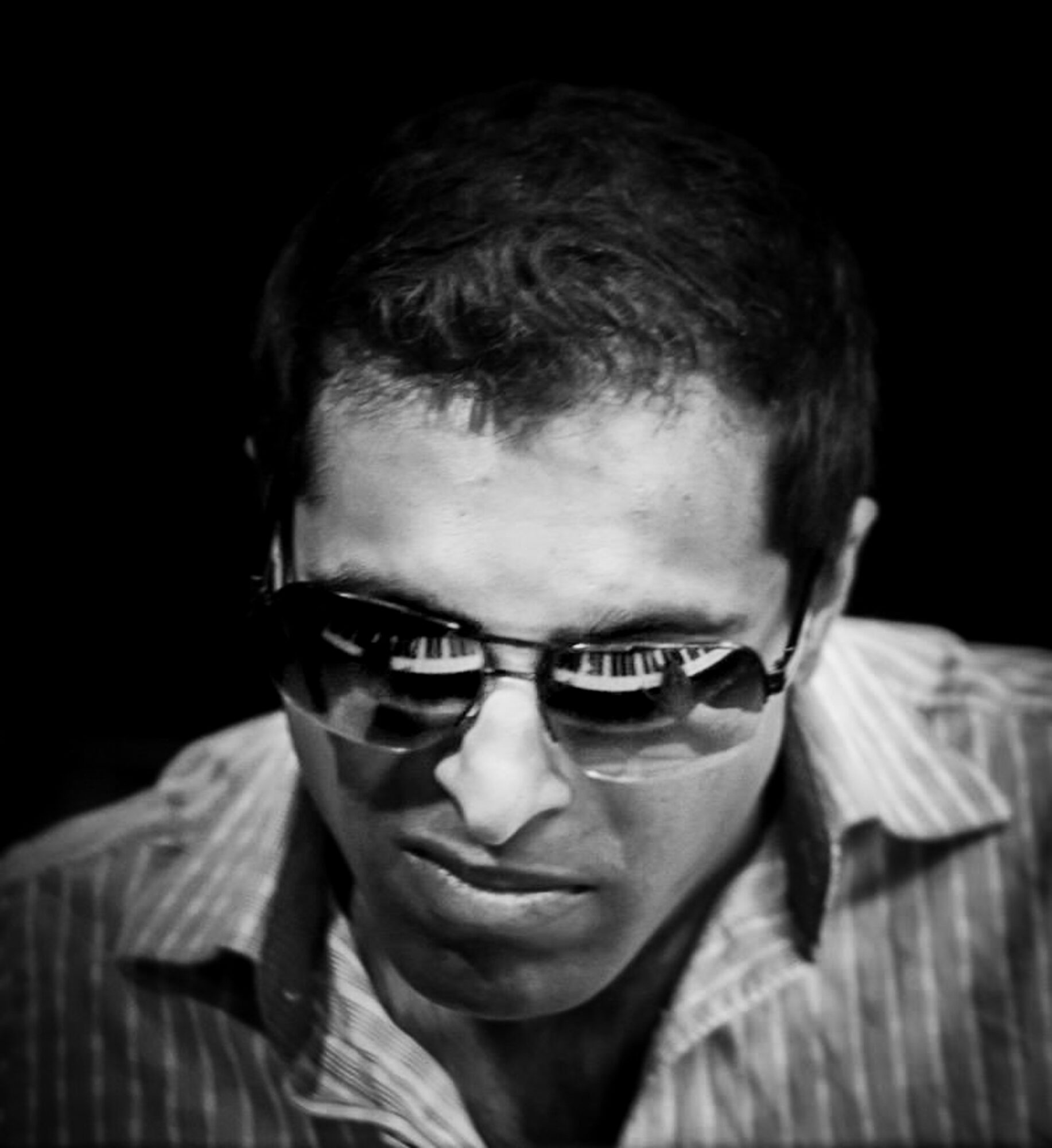 Man wearing sunglasses and a striped shirt, looking downward, in black and white.