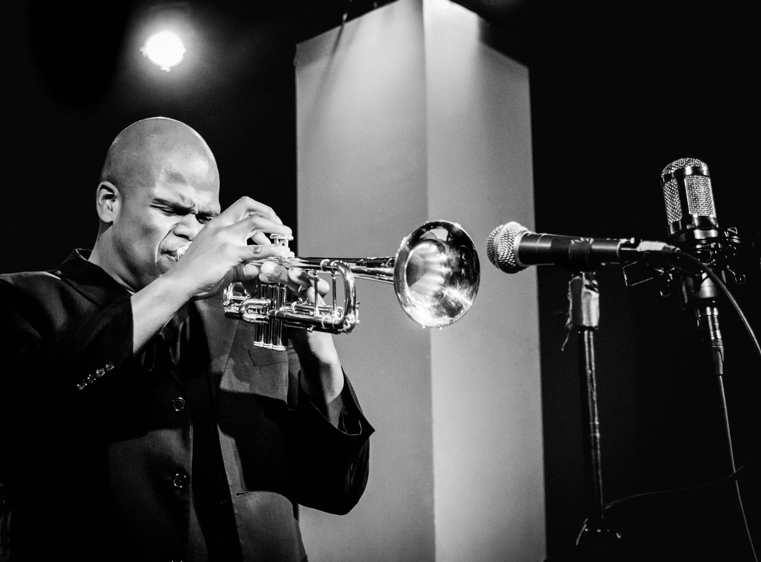 Person playing trumpet in a recording studio with microphone, black and white image.