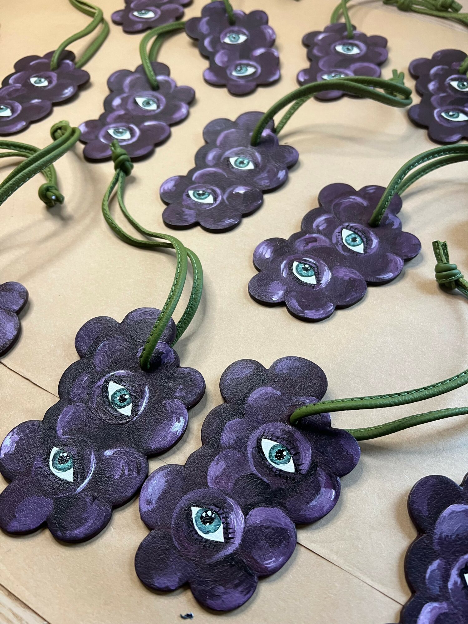 Multiple purple flower-shaped objects with blue eyes attached to green cords, arranged on a beige surface.