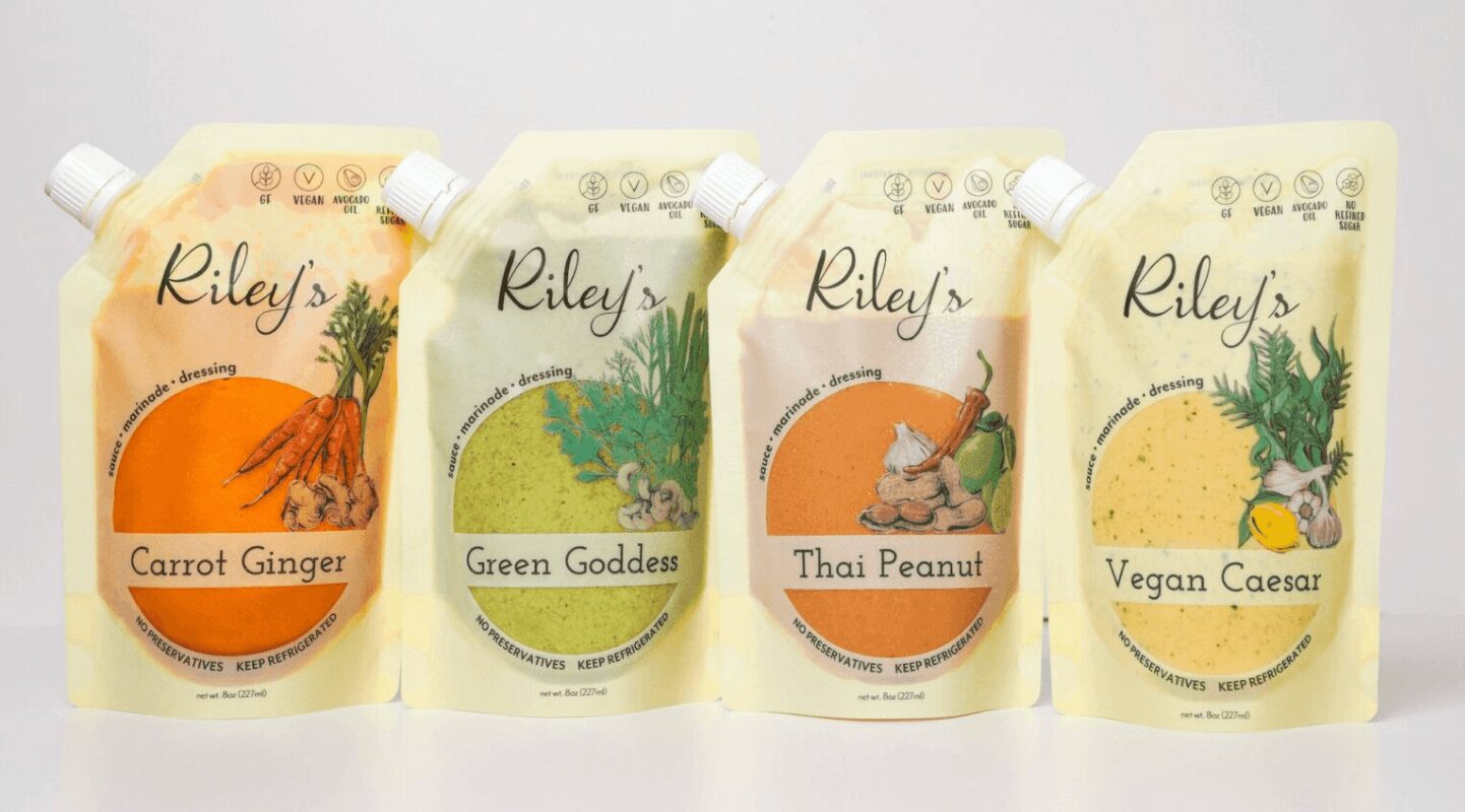Four Riley's plant-based food pouches with different flavors: Carrot Ginger, Green Goddess, Thai Peanut, Vegan Caesar, arranged in a row.