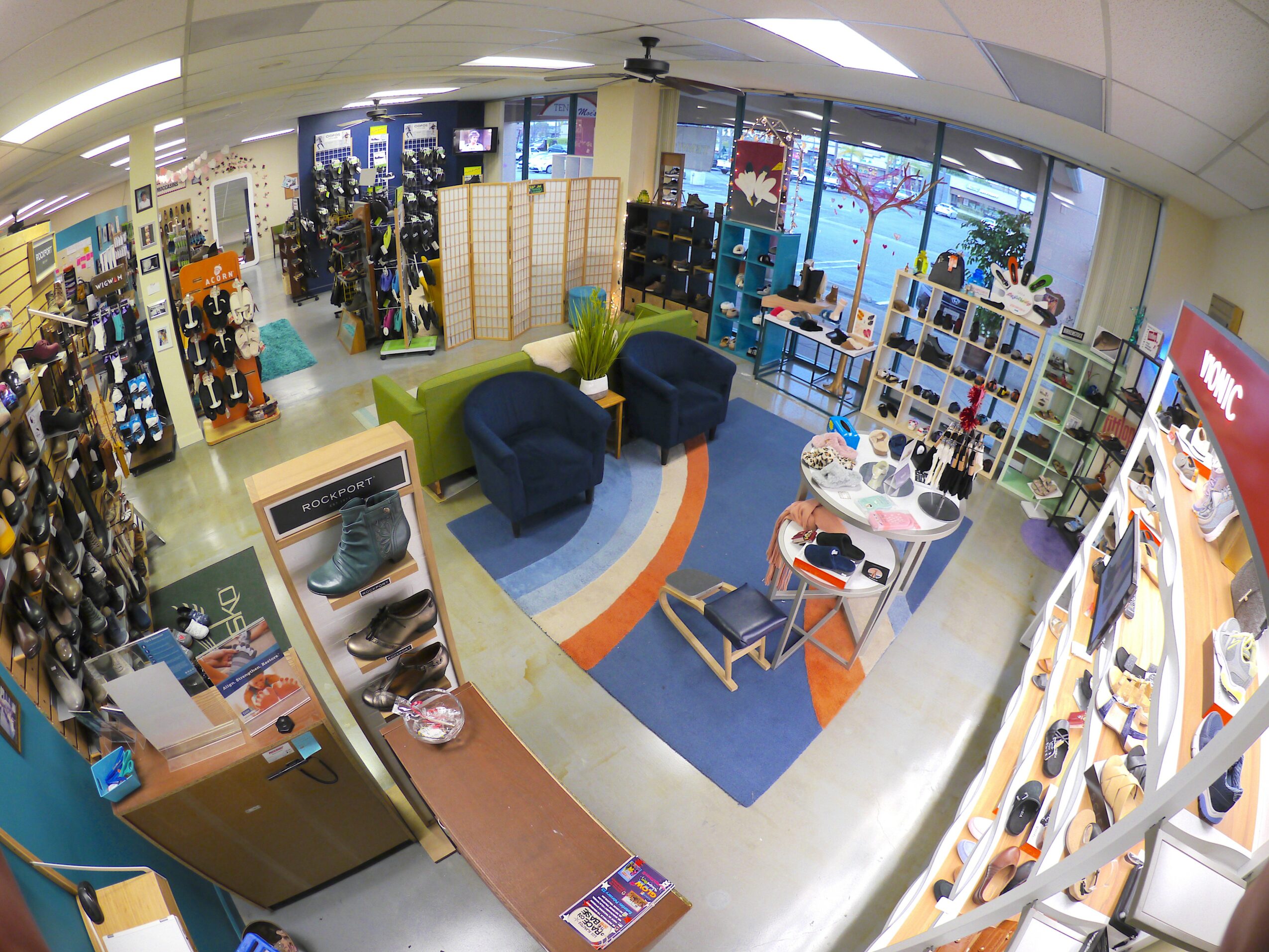 Store interior with seating area, shelves of shoes, and large windows, viewed from an elevated angle.