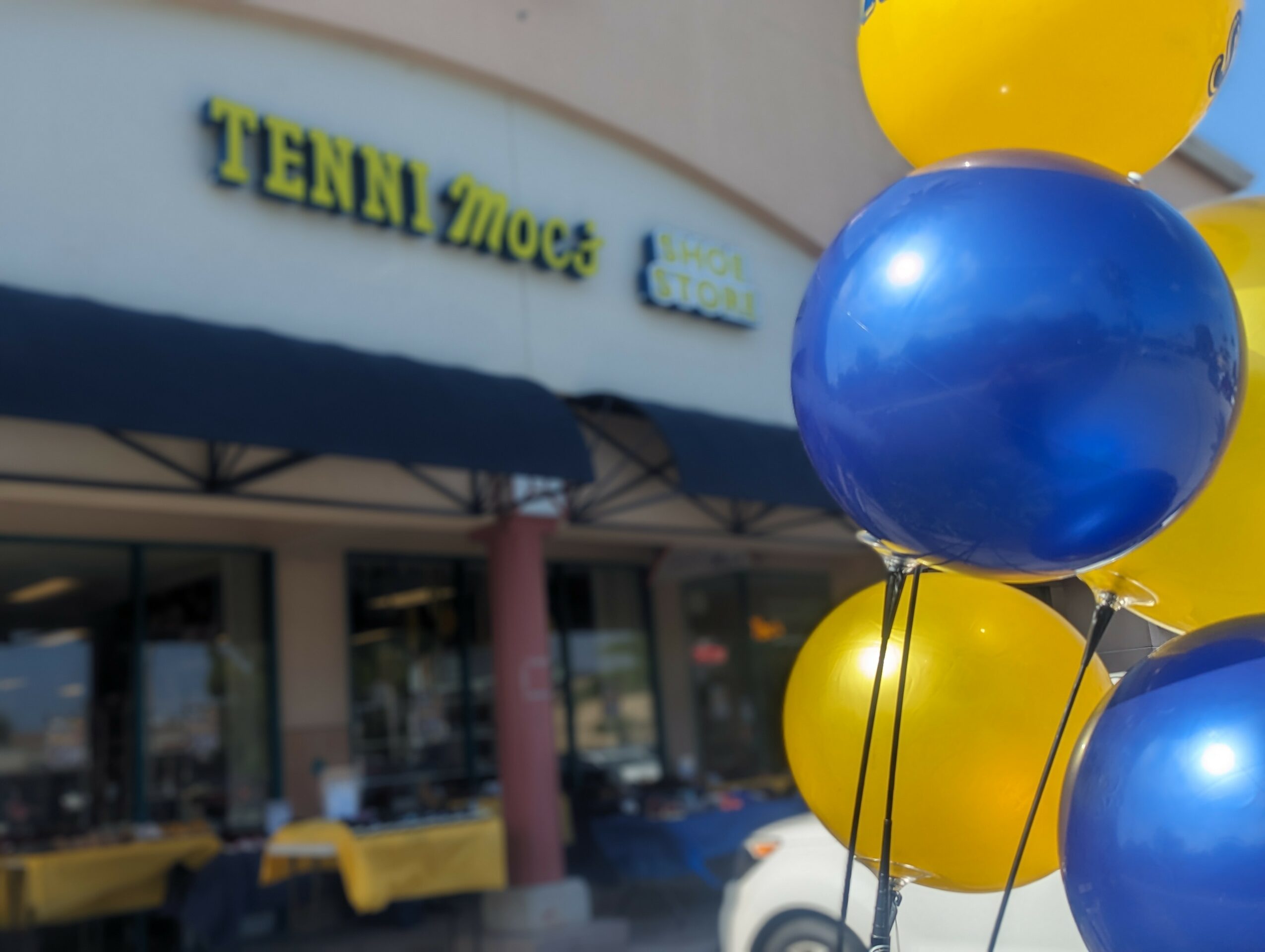 Blue and yellow balloons in front of a store with a sign reading 'TENN MOES'.