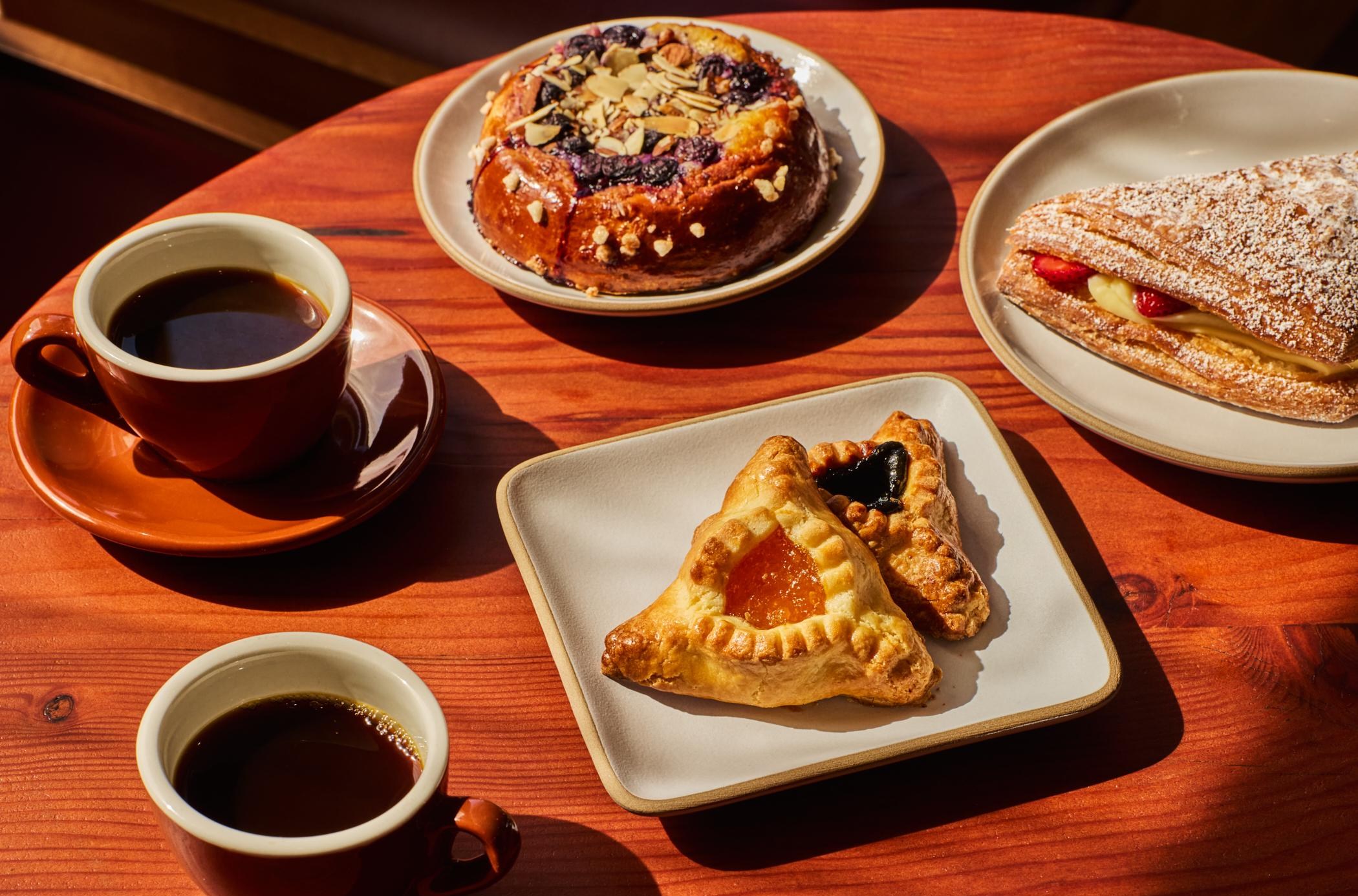 A couple of cups of coffee on a table with pastries.