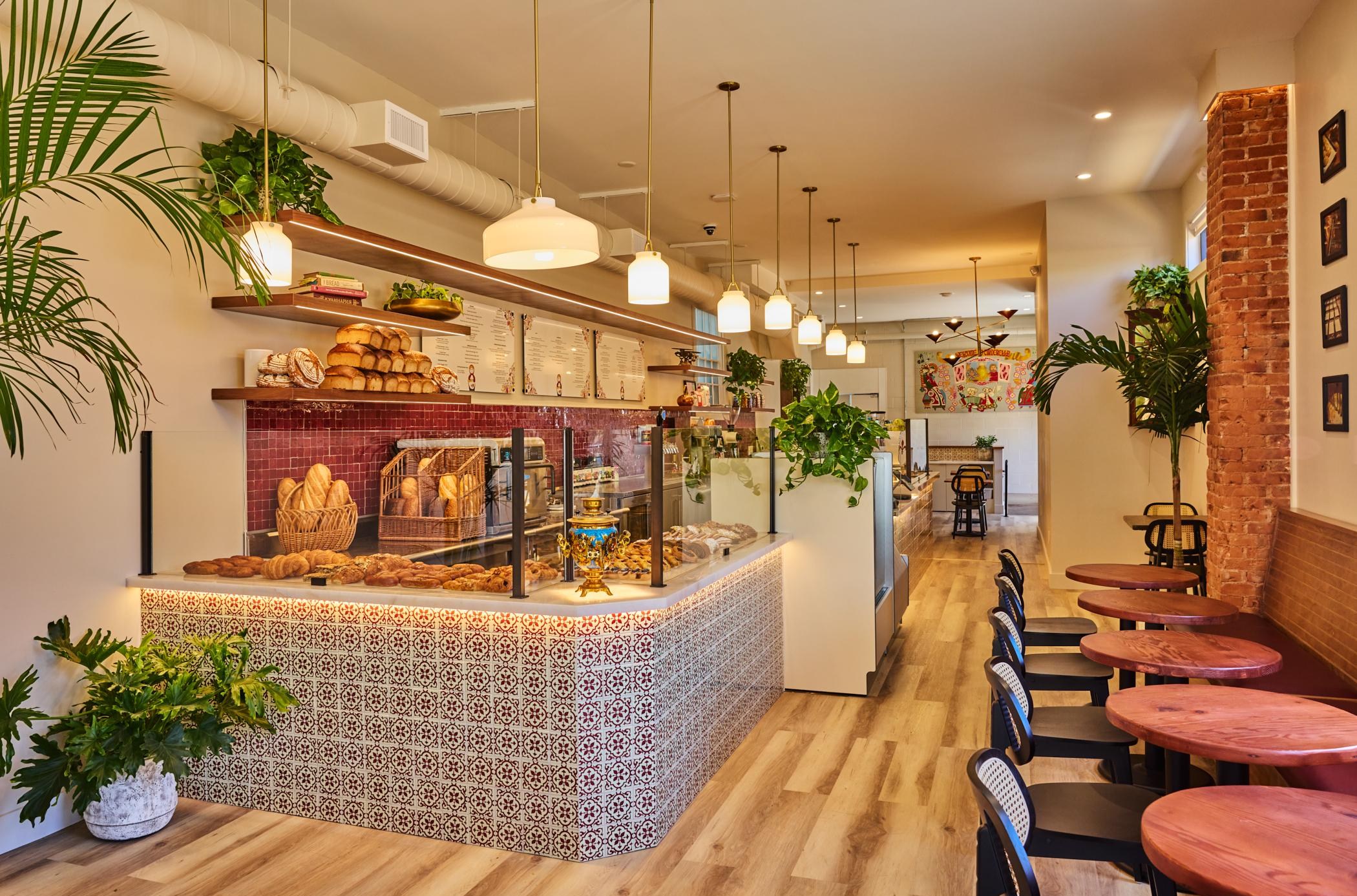 A wide view of the pastry counter and circular tables with chairs and a banquette.