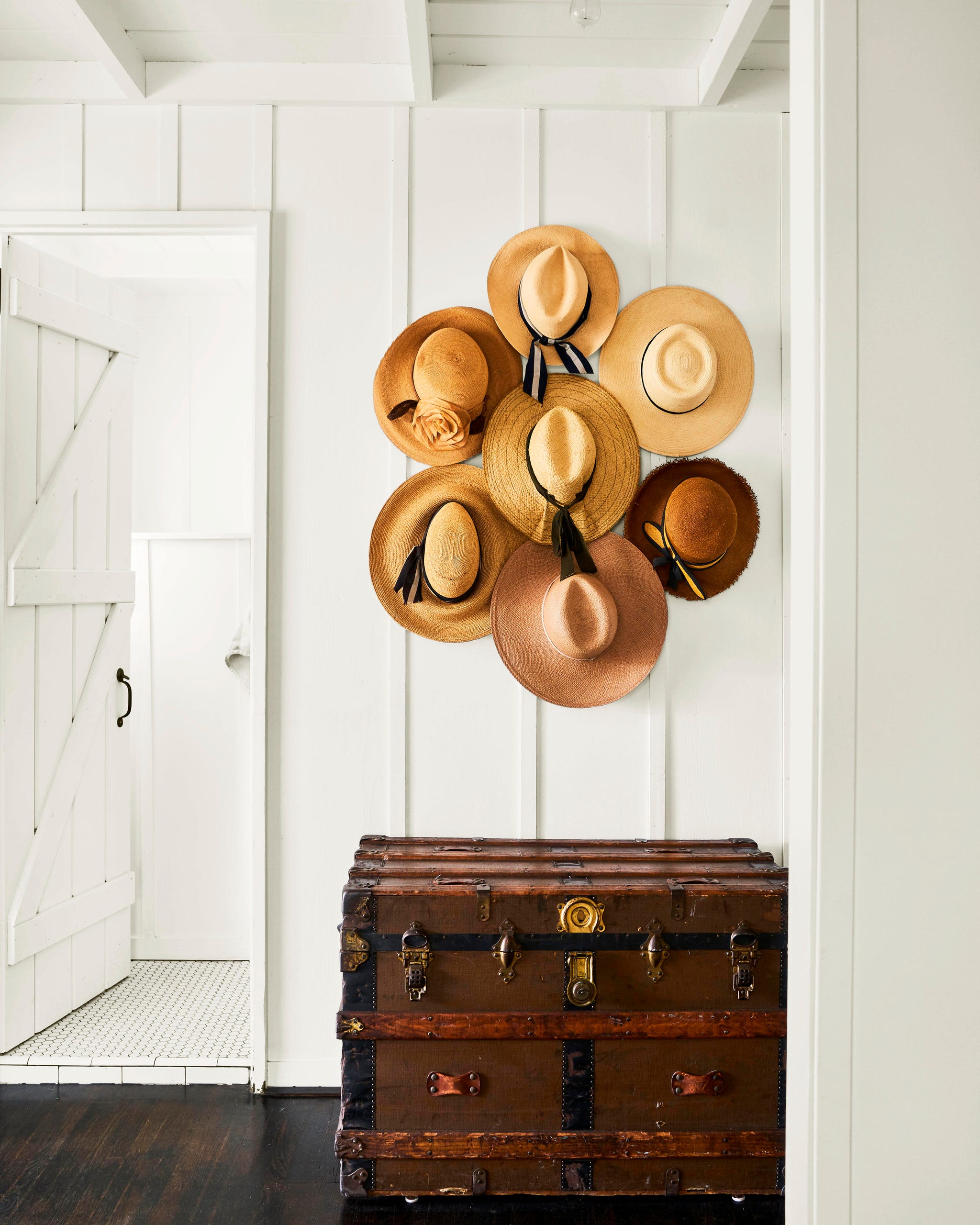 hat collection hung on a white wall with a wooden trunk under it hat collection hung on a white wall with a wooden trunk under it