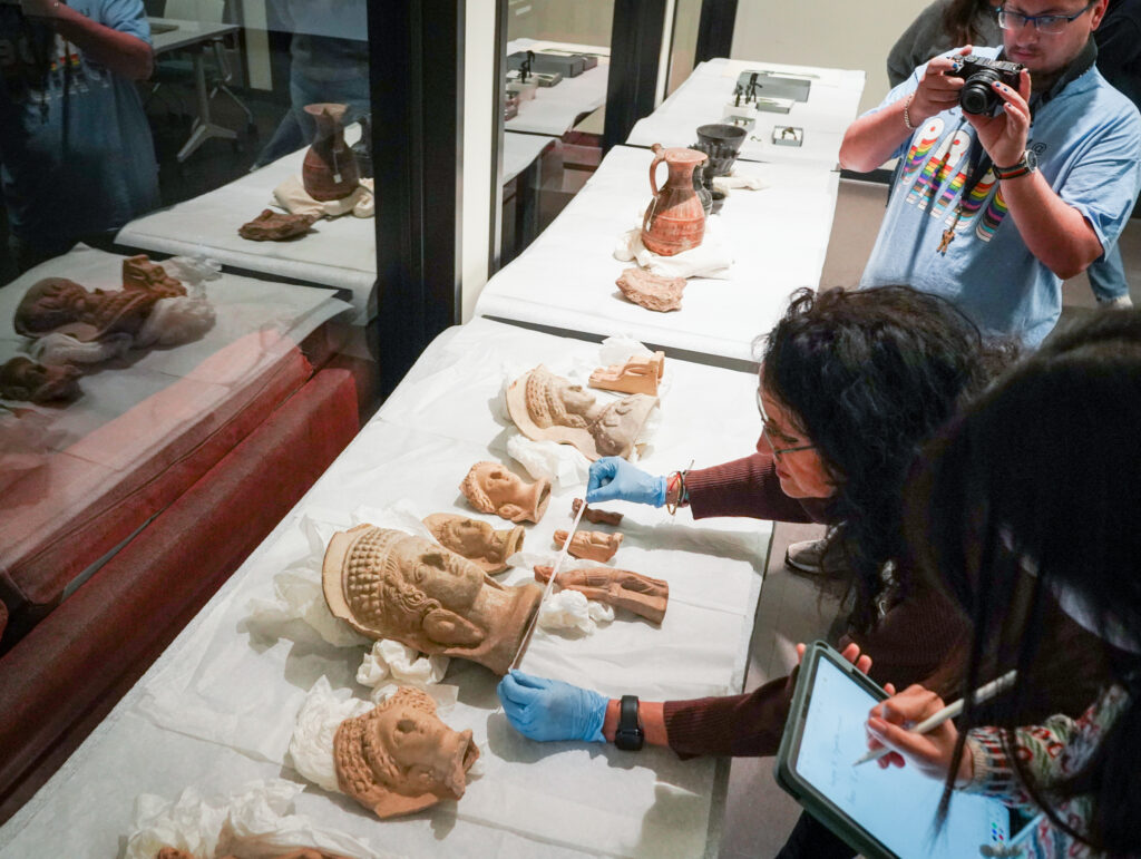 Students look at Etruscan items from the Hearst Museum on March 4, 2025, in preparation for an exhibit in the Brown Gallery of Doe Library in 2026. A student takes notes on an iPad while Pieraccini makes measurements.