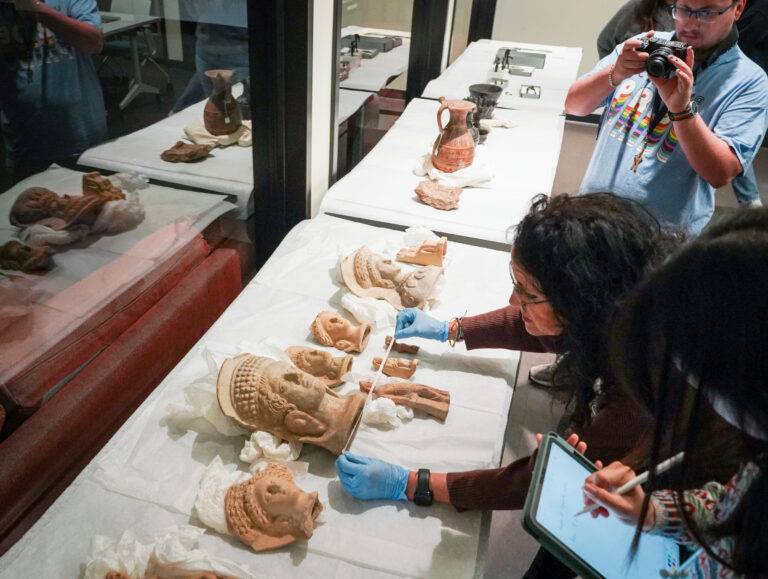 Students look at Etruscan items from the Hearst Museum on March 4, 2025, in preparation for an exhibit in the Brown Gallery of Doe Library in 2026. A student takes notes on an iPad while Pieraccini makes measurements.