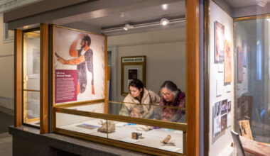 Two people lean over a glass display case, arranging artifacts for an exhibit about the anciet Etruscans at in the Doe Library lobby.