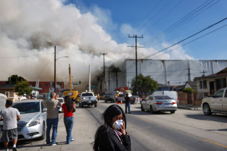 A person wears a face mask as a massive warehouse fire at a cold storage facility continues to burn and spread smoke around the city on June 20, 2026, in Los Angeles, California.