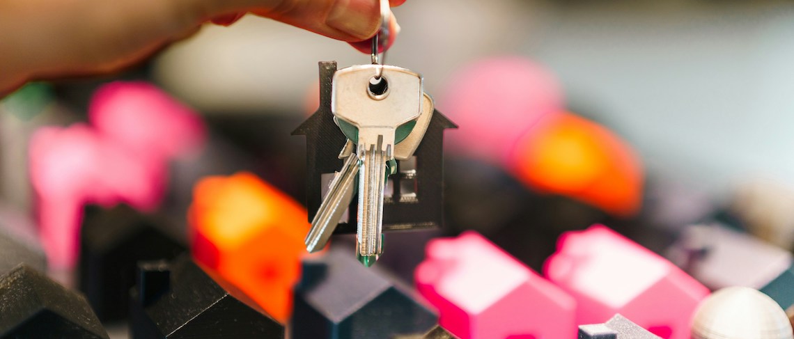 A pair of house keys dangling over multicolored miniature home figures