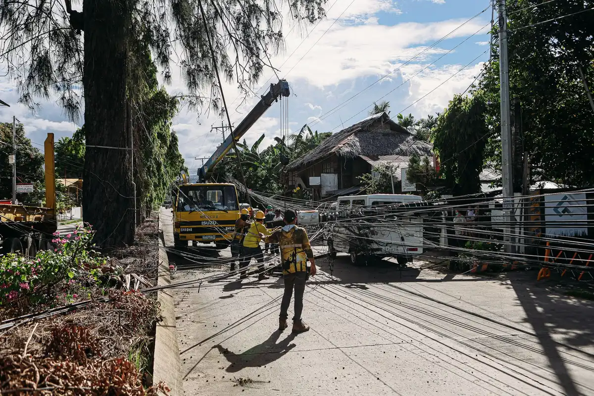 Utility repair crew working on electrical lines with bucket truck elevated against morning sky, orange safety vests, focused on overhead power line repairs