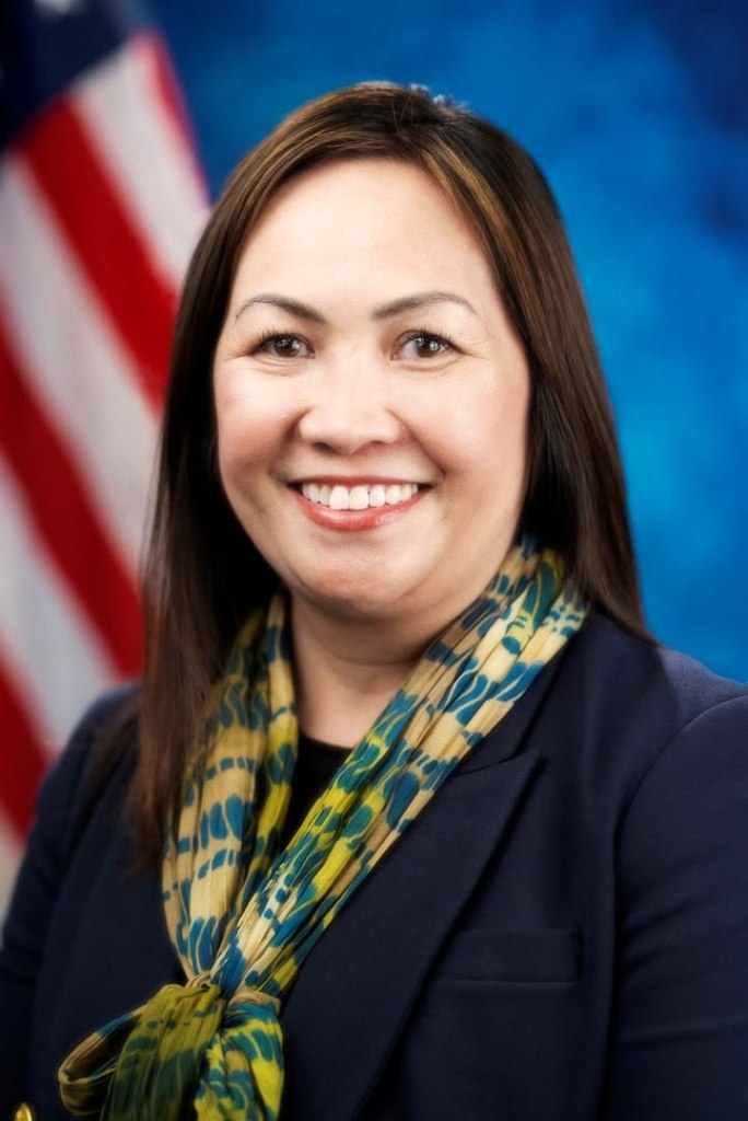 Mao Misty Her, deputy superintendent of a California school district, smiles against the backdrop of an American flag.