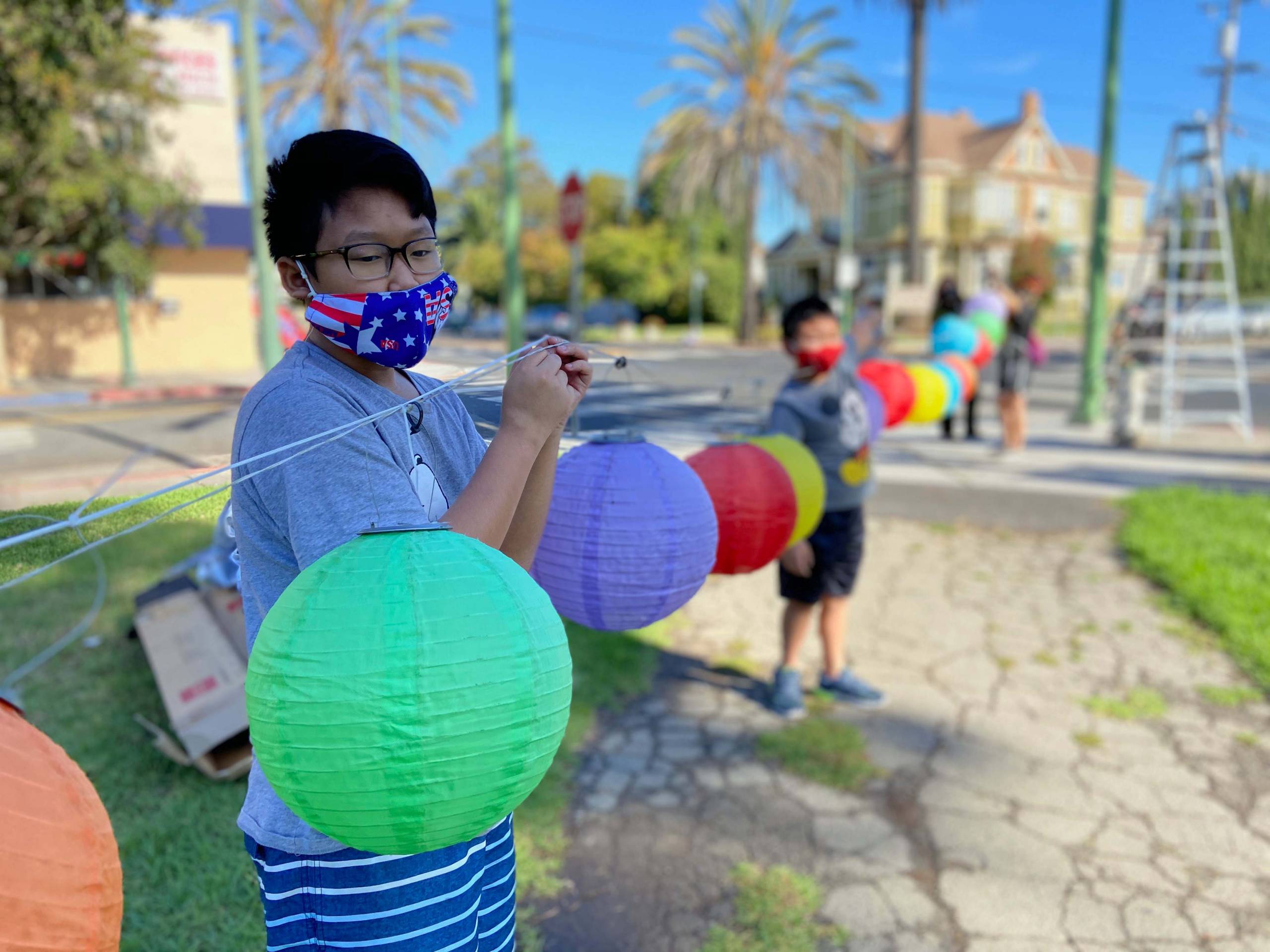 Schoolchildren in face masks stringing up paper lanterns in Clinton Park, Oakland.