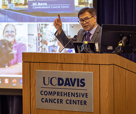 Primo "Lucky" Lara, Jr., cancer center director, at a podium, with his hand raised
